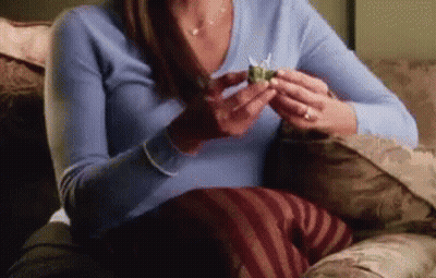 A Woman Is Sitting On A Couch Holding A Small Object In Her Hand . GIF