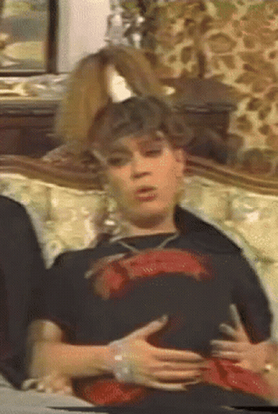 A Woman Is Sitting On A Couch Holding Her Belly GIF