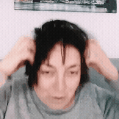 A Woman Is Sitting On A Couch Holding Her Hair In Her Hands . GIF