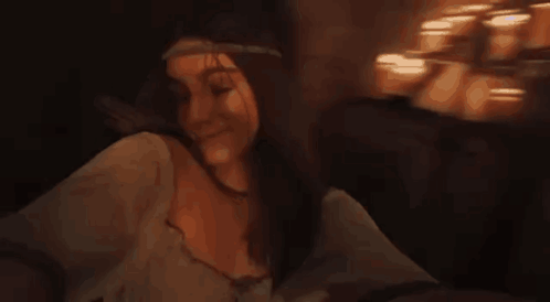 A Woman Is Sitting On A Couch In A Dark Room With Candles In The Background . GIF