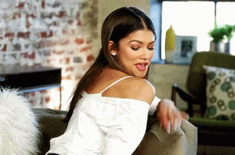 A Woman Is Sitting On A Couch In A Living Room Looking Over Her Shoulder . GIF