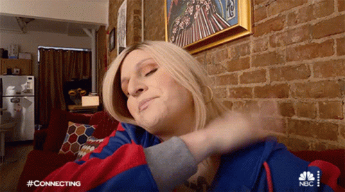 A Woman Is Sitting On A Couch In Front Of A Brick Wall Wearing A Nbc Hoodie GIF