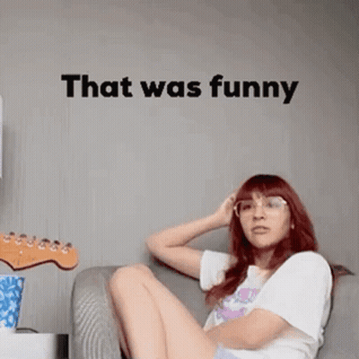 A Woman Is Sitting On A Couch In Front Of A Wall With The Words `` That Was Funny '' . GIF