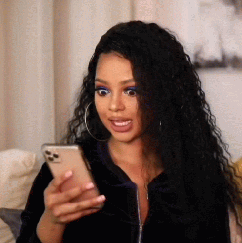 A Woman Is Sitting On A Couch Looking At Her Phone And Making A Funny Face . GIF