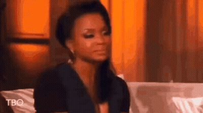 A Woman Is Sitting On A Couch Making A Funny Face And Looking At The Camera . GIF