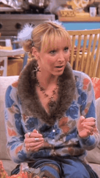 A Woman Is Sitting On A Couch Wearing A Floral Cardigan And A Fur Collar . GIF
