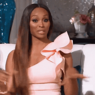 A Woman Is Sitting On A Couch Wearing A Pink Dress With Ruffles On The Shoulder . GIF