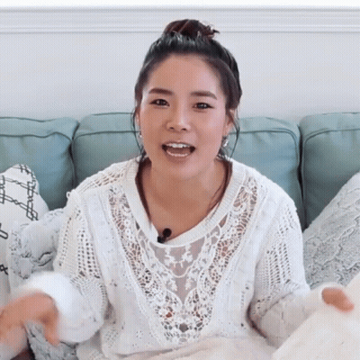 A Woman Is Sitting On A Couch Wearing A White Sweater GIF