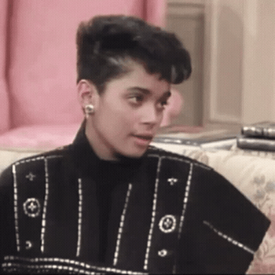 A Woman Is Sitting On A Couch Wearing Earrings And A Black Jacket . GIF