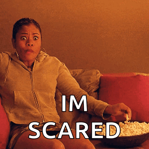 A Woman Is Sitting On A Couch With A Bowl Of Popcorn And The Words Im Scared Below Her GIF