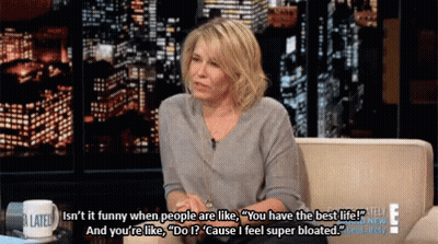 A Woman Is Sitting On A Couch With A Cup That Says A Late Show On It GIF