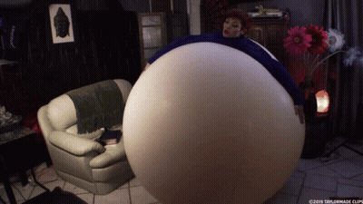A Woman Is Sitting On A Couch With A Large Balloon Around Her Belly GIF