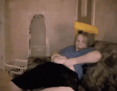 A Woman Is Sitting On A Couch With A Pillow On Her Head And A Yellow Pillow On Her Head . GIF