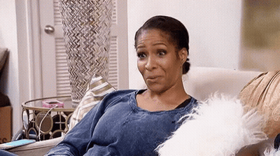 A Woman Is Sitting On A Couch With A White Pillow And A Cell Phone . GIF