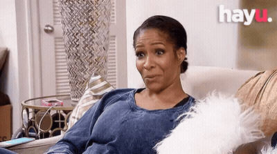 A Woman Is Sitting On A Couch With A White Pillow And A Phone . GIF
