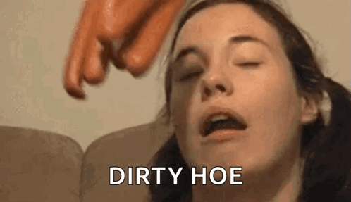 A Woman Is Sitting On A Couch With Her Eyes Closed And A Person Is Pointing At Her Face With A Sausage . GIF