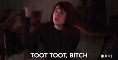A Woman Is Sitting On A Couch With Her Fist In The Air And Saying Toot Toot Bitch . GIF
