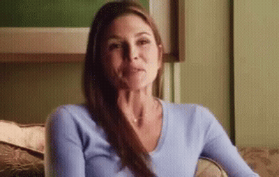 A Woman Is Sitting On A Couch With Her Hand On Her Chin And Looking At The Camera . GIF