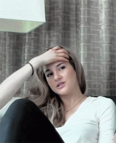A Woman Is Sitting On A Couch With Her Hand On Her Head GIF