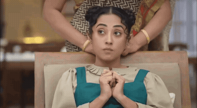 A Woman Is Sitting On A Couch With Her Hands On Her Neck While Another Woman Holds Her Hair . GIF