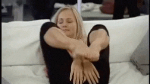 A Woman Is Sitting On A Couch With Her Legs Crossed And Her Hands On Her Hips . GIF
