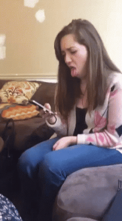 A Woman Is Sitting On A Couch With Her Tongue Out And Looking At Her Phone GIF