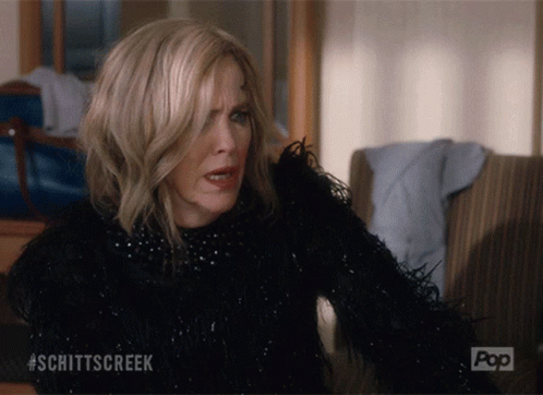 A Woman Is Sitting On A Couch With #Schittscreek Written On The Bottom GIF