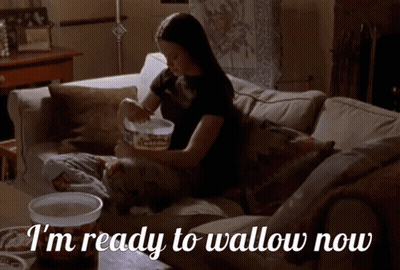 A Woman Is Sitting On A Couch With The Words I 'M Ready To Wallow Now GIF