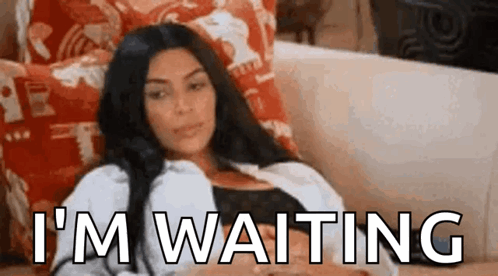 A Woman Is Sitting On A Couch With The Words `` I 'M Waiting '' Written Above Her . GIF