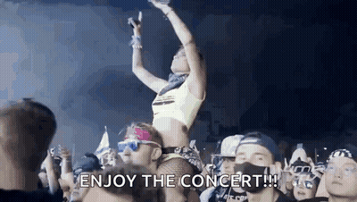 A Woman Is Sitting On A Man 'S Shoulders At A Concert Holding A Microphone . GIF