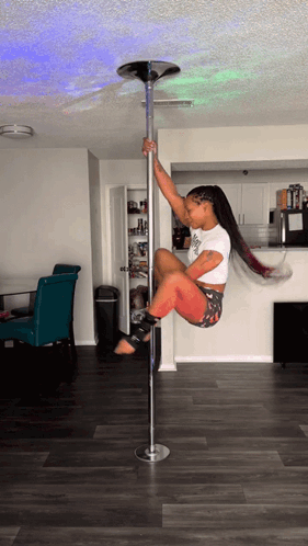 A Woman Is Sitting On A Pole In A Living Room Wearing A White Shirt That Says ' Swag ' On It GIF