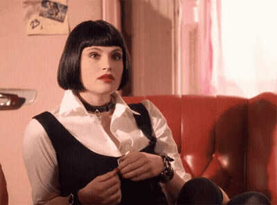 A Woman Is Sitting On A Red Couch Wearing A Choker And A Wig . GIF
