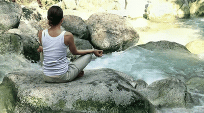 A Woman Is Sitting On A Rock In Front Of A River In A Lotus Position . GIF