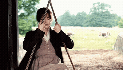 A Woman Is Sitting On A Rope Swing In A Field With Sheep In The Background GIF