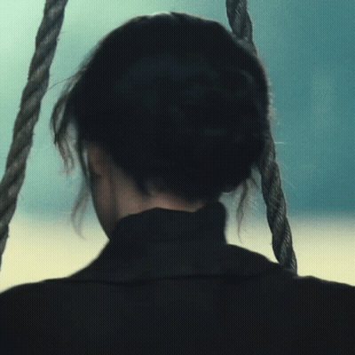 A Woman Is Sitting On A Rope Swing Looking Out Over The Ocean GIF