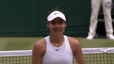 A Woman Is Sitting On A Tennis Court Wearing A Hat And Smiling . GIF
