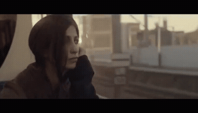 A Woman Is Sitting On A Train Looking Out The Window At The City . GIF