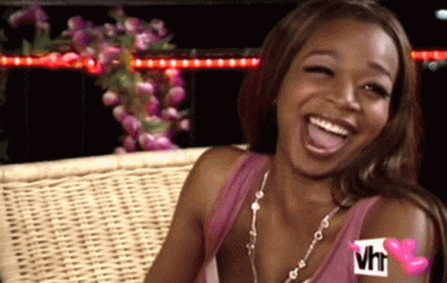 A Woman Is Sitting On A Wicker Bench Laughing With A Vh1 Logo On Her Arm . GIF