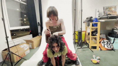 A Woman Is Sitting On Another Woman 'S Back In A Room With Boxes And A Bag That Says Goku On It GIF