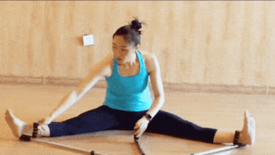 A Woman Is Sitting On The Floor Stretching Her Legs With A Pair Of Poles . GIF