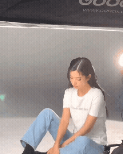 A Woman Is Sitting On The Floor Wearing A White T-Shirt That Says Calvin Klein Jeans . GIF