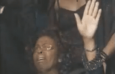 A Woman Is Sitting On The Floor With Her Hands In The Air And A Man Is Standing Behind Her . GIF