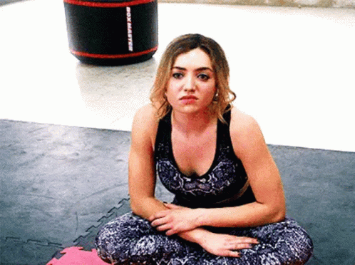 A Woman Is Sitting On The Floor With Her Legs Crossed In A Gym . GIF