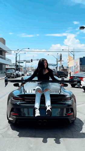 A Woman Is Sitting On The Hood Of A Sports Car GIF