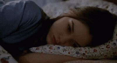 A Woman Is Sleeping On A Bed With A Floral Comforter . GIF