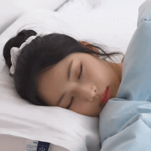 A Woman Is Sleeping On A Bed With A Pillow That Says Cool & Glow GIF