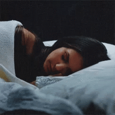 A Woman Is Sleeping On A Bed With A White Blanket GIF