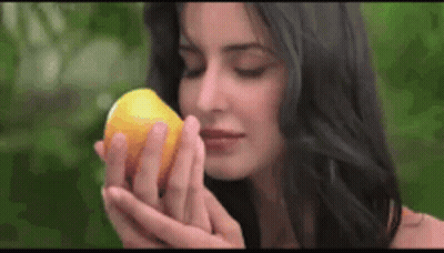 A Woman Is Smelling A Lemon In Her Hand . GIF