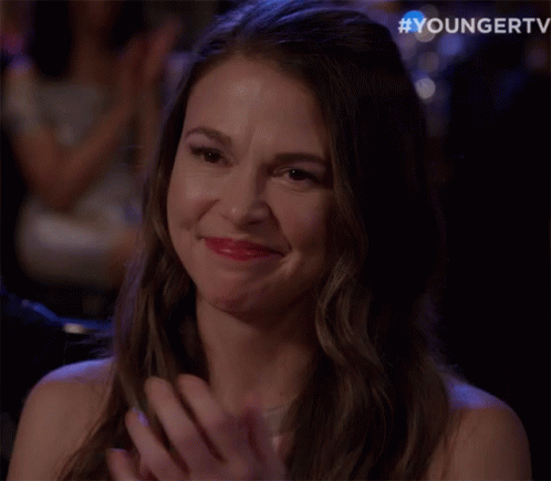 A Woman Is Smiling And Clapping Her Hands In A Crowd Of People . GIF