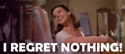 A Woman Is Smiling And Dancing In A Room With The Words `` I Regret Nothing '' Written On The Bottom . GIF